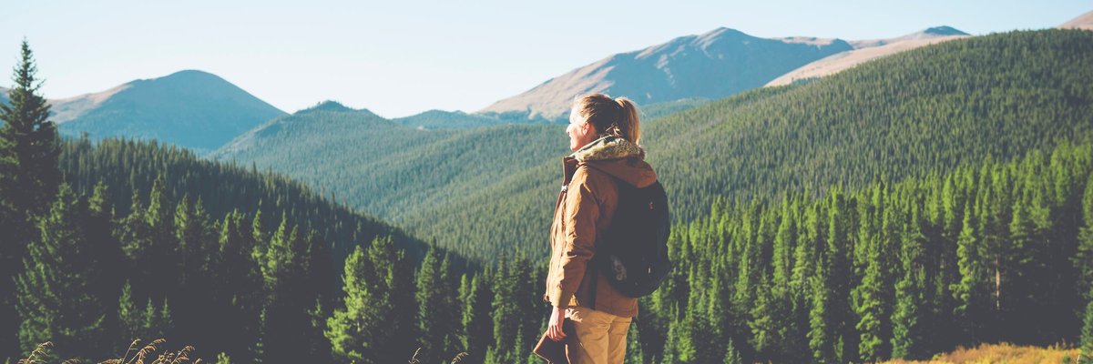 A hiker standing at the top of an open space and admiring the view of the mountains and trees.