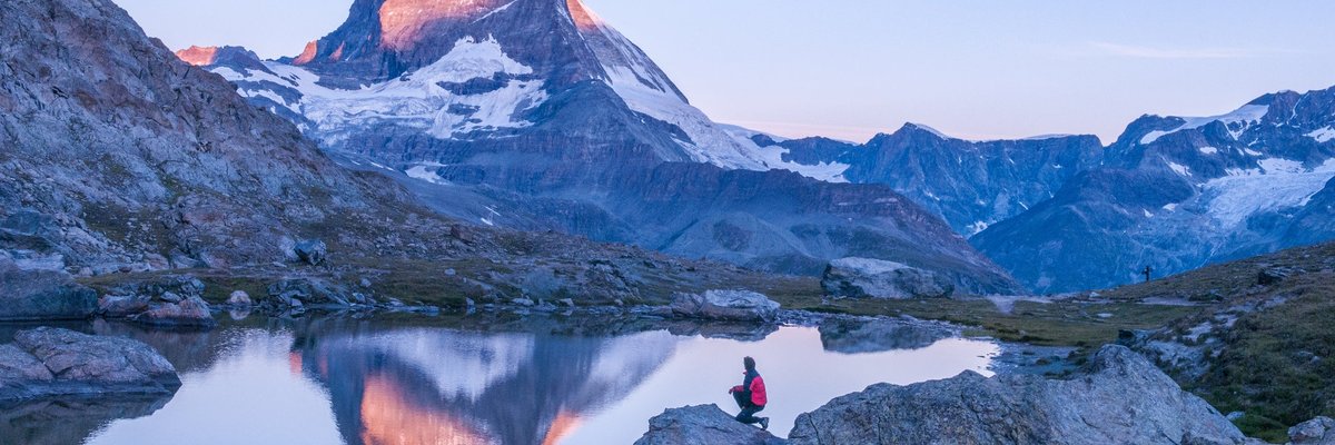 A hiker standing next to a lake looking at the sun hitting the top of the Matterhorn peak in Switzerland.