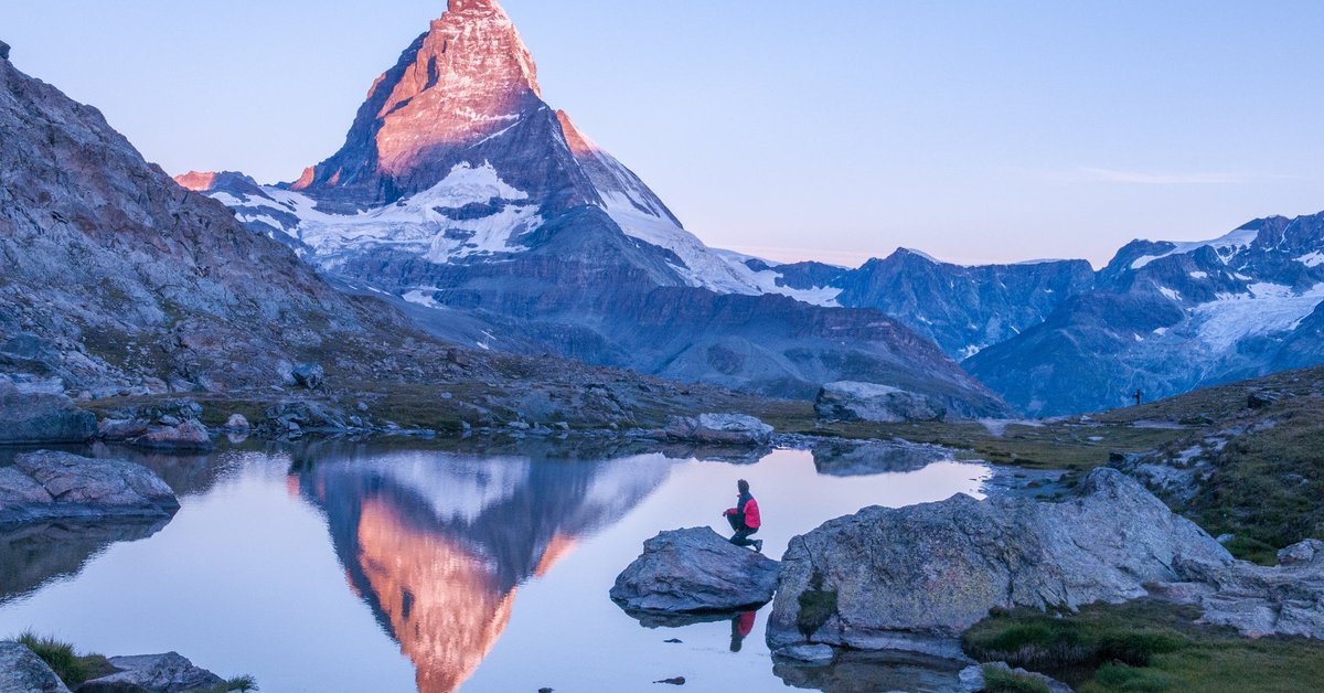 A hiker standing next to a lake looking at the sun hitting the top of the Matterhorn peak in Switzerland.