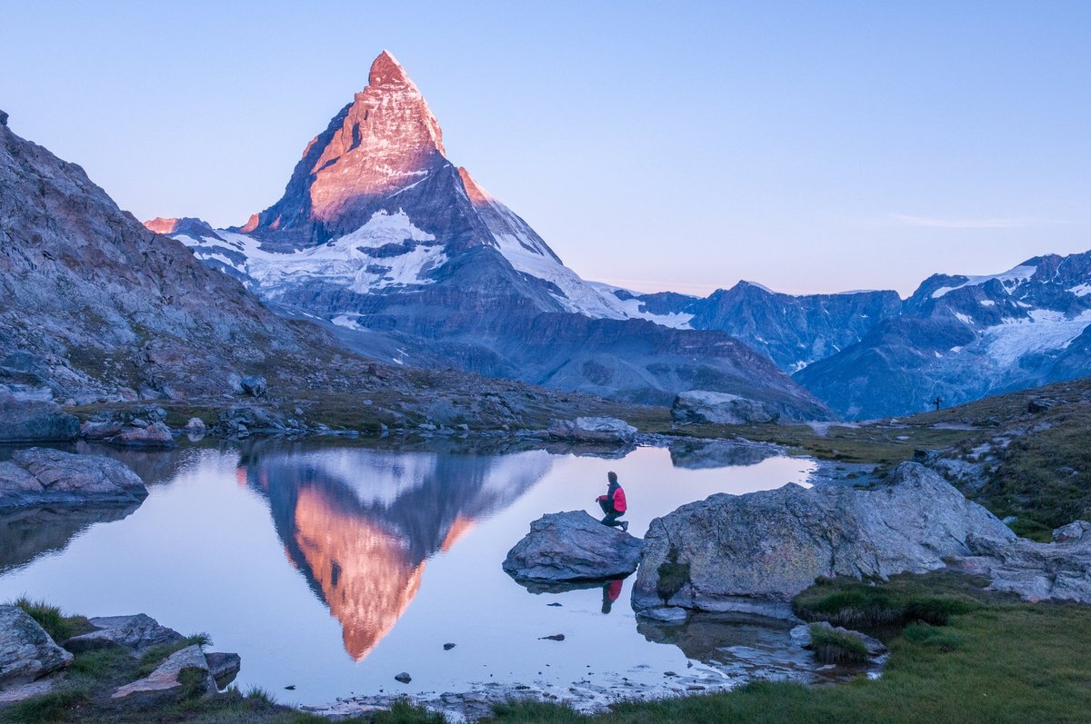 A hiker standing next to a lake looking at the sun hitting the top of the Matterhorn peak in Switzerland.