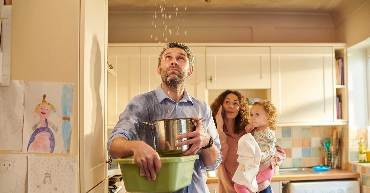 Man standing below leaky ceiling catching water in a bucket.