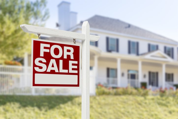 A For Sale sign in front of a sunny green lawn and white two-story home.