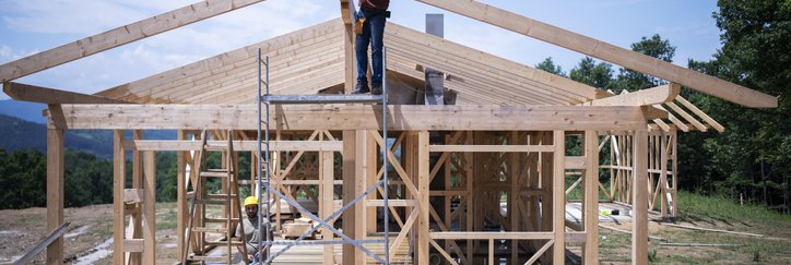 The frame of a house under construction with workers on site.