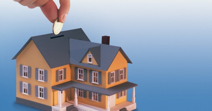 A hand drops money into a house-shaped coin bank