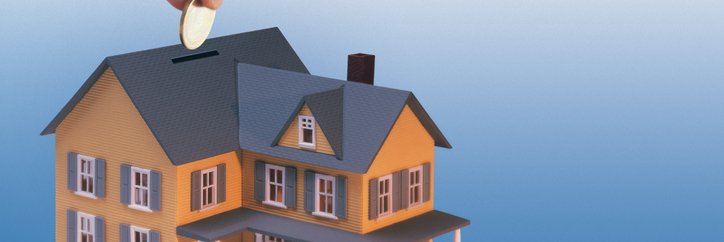 A hand drops money into a house-shaped coin bank