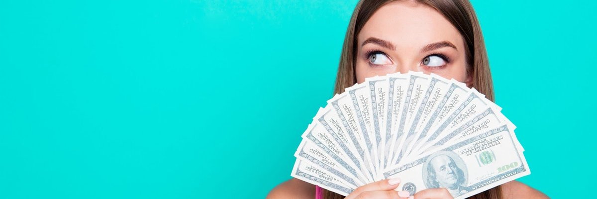 Young woman holding a fan of hundred-dollar bills in front of her face.
