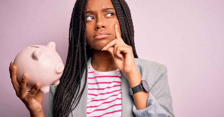 A puzzled woman holds a piggy bank