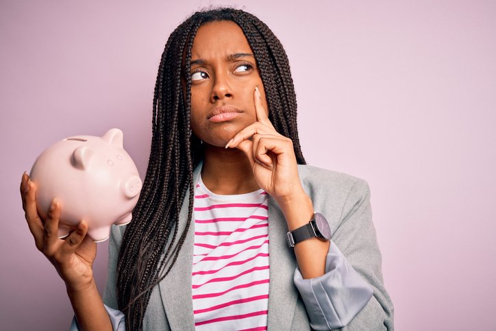 A puzzled woman holds a piggy bank
