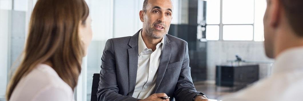 A business man in conversation with two people at a desk in an office