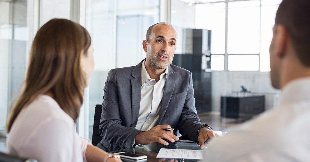 A business man in conversation with two people at a desk in an office