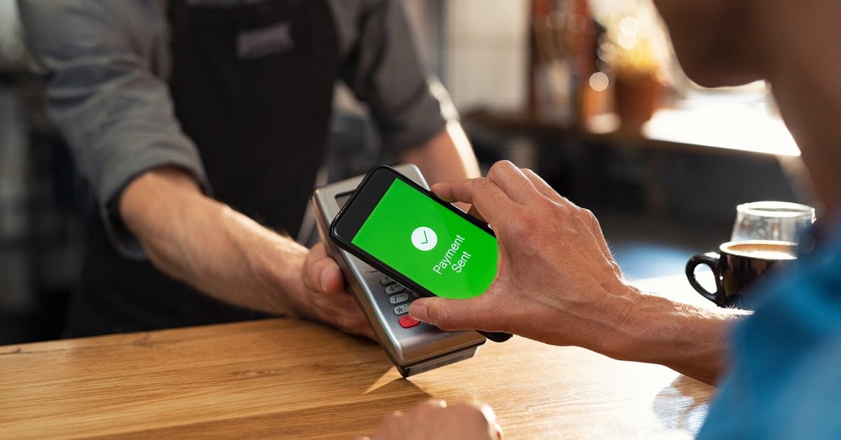 person in store paying with mobile wallet holding phone up to contact point with the screen displaying payment sent