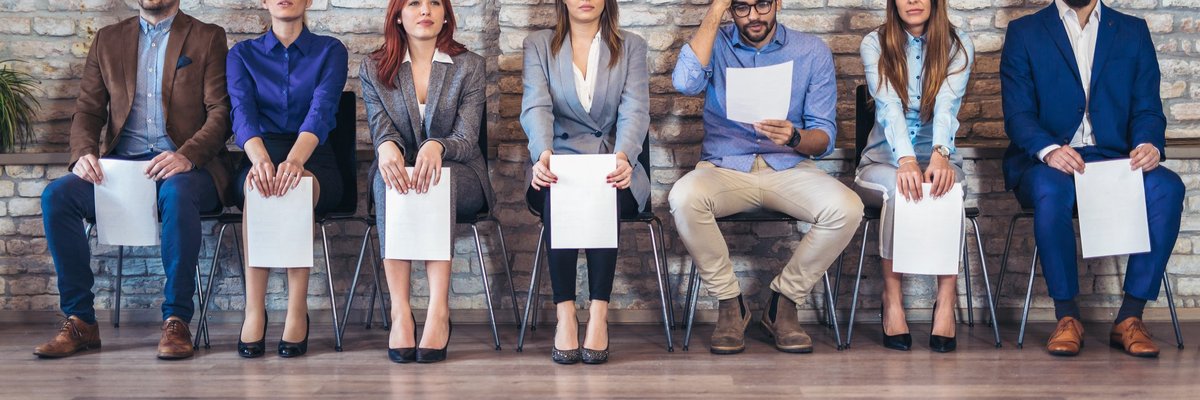 A line of people seated waiting for an interview with resumes in hand.