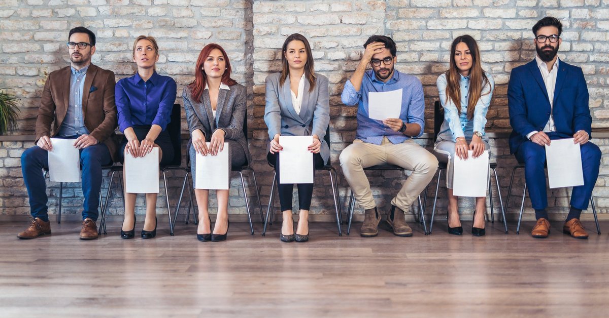 A line of people seated waiting for an interview with resumes in hand.