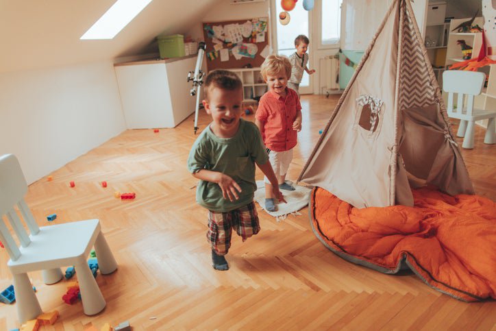 Three young children playing in a colorful room filled with toys and a canvas tent.