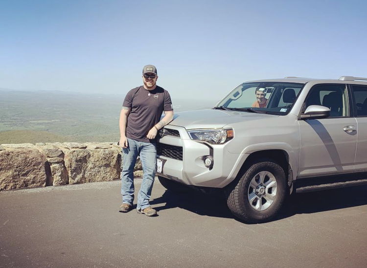 Man leaning on a Toyota SUV with a scenic view in the background.