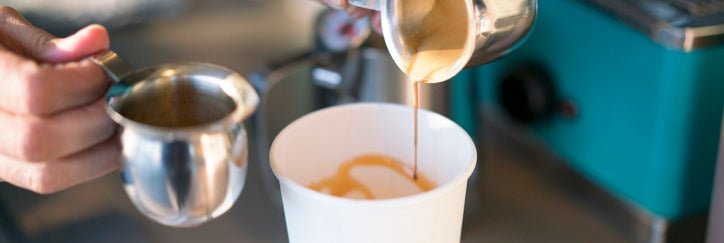 A barista making a latte in a takeout coffee cup.