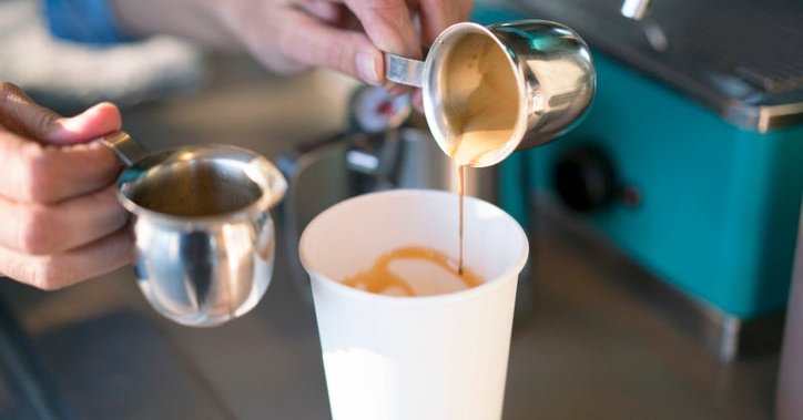 A barista making a latte in a takeout coffee cup.