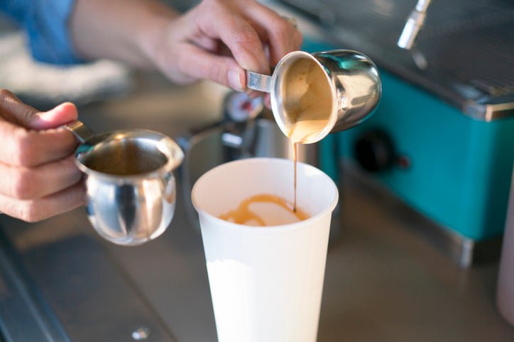 A barista making a latte in a takeout coffee cup.