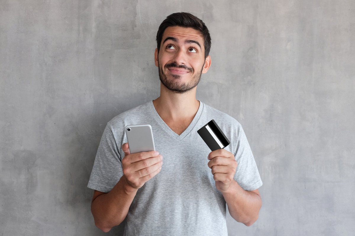 Smiling man in gray shirt holding a cell phone and a credit card