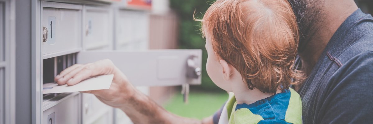 A man holding his baby while opening a mailbox and removing an envelope.