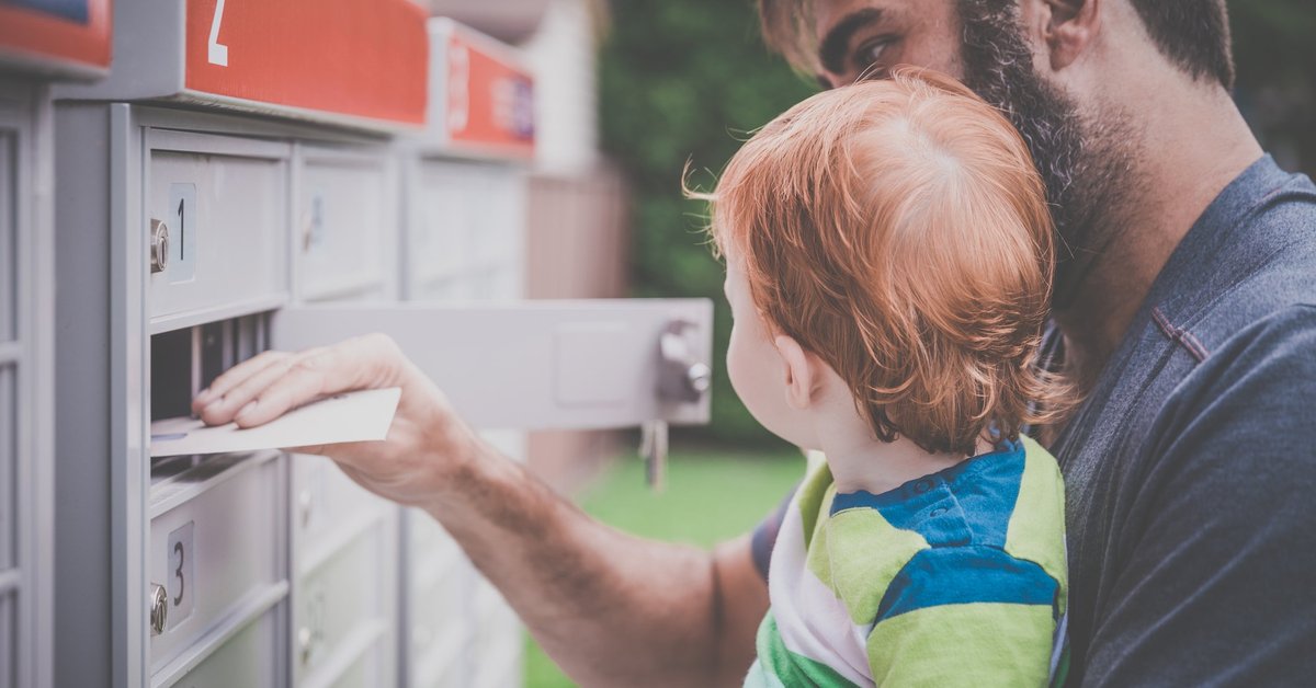 A man holding his baby while opening a mailbox and removing an envelope.