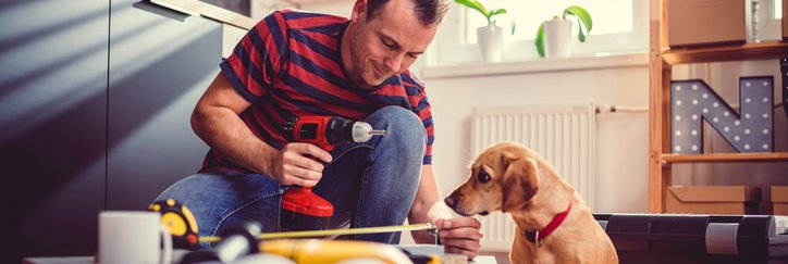 A man measuring new cabinets that he's installing in his kitchen while his dog sits next to him and watches.