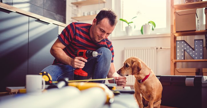 A man measuring new cabinets that he's installing in his kitchen while his dog sits next to him and watches.