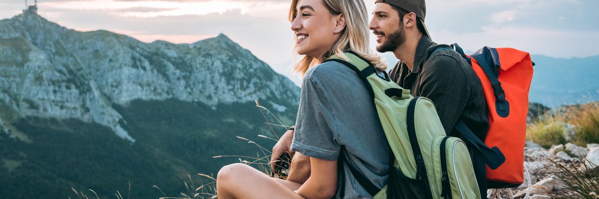 A man and woman resting and enjoying the view with backpacks on after completing a hike to a mountaintop.