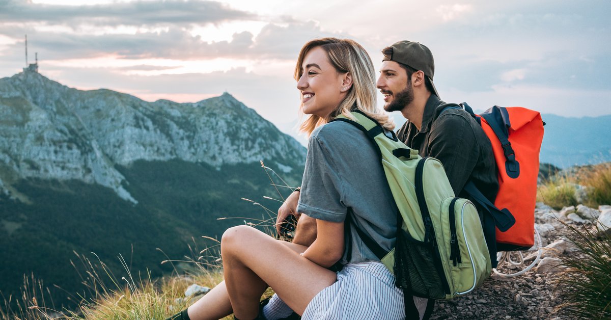 A man and woman resting and enjoying the view with backpacks on after completing a hike to a mountaintop.