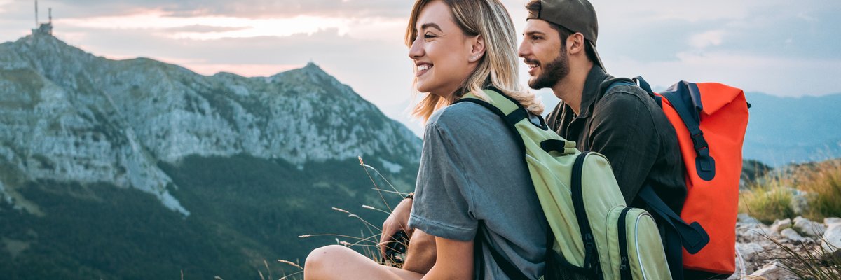 A man and woman resting and enjoying the view with backpacks on after completing a hike to a mountaintop.