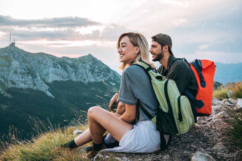 A man and woman resting and enjoying the view with backpacks on after completing a hike to a mountaintop.