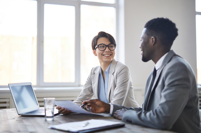 A man and woman in a client meeting speaking and pointing at documents.