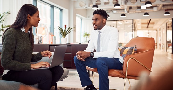 A woman asking a man questions in a job interview in a casual office setting.
