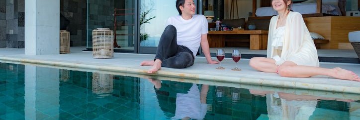 A man and woman sitting at the edge of a pool outside their room in a luxury hotel.