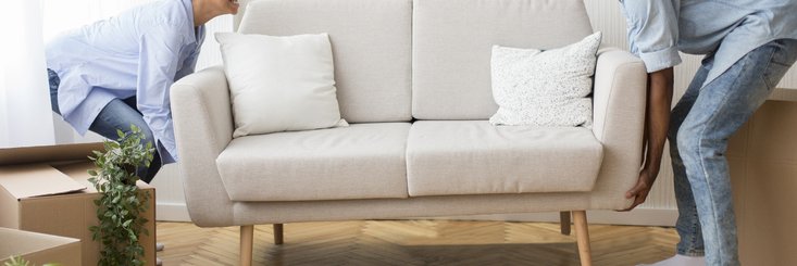 A man and woman moving a new couch into their living room.