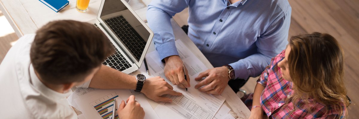 man and woman sitting across desk from man in business attire looking at financial documents
