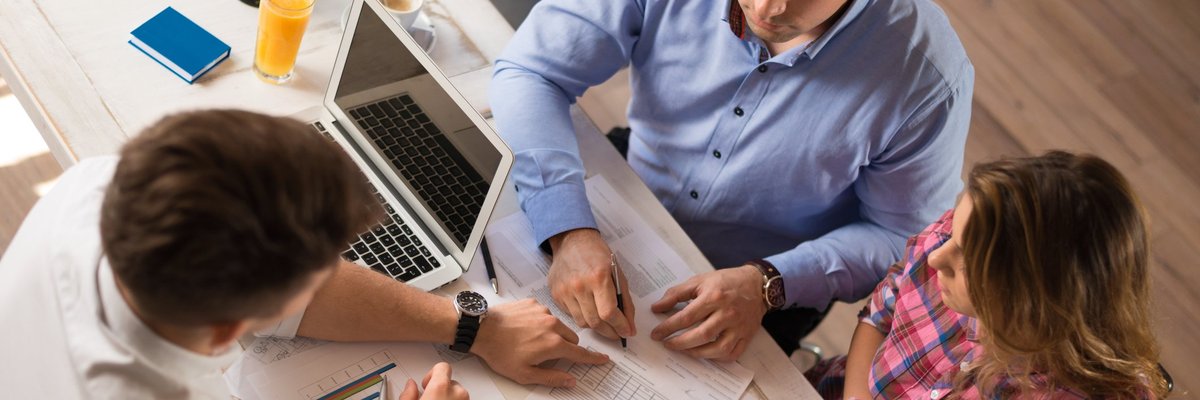 man and woman sitting across desk from man in business attire looking at financial documents