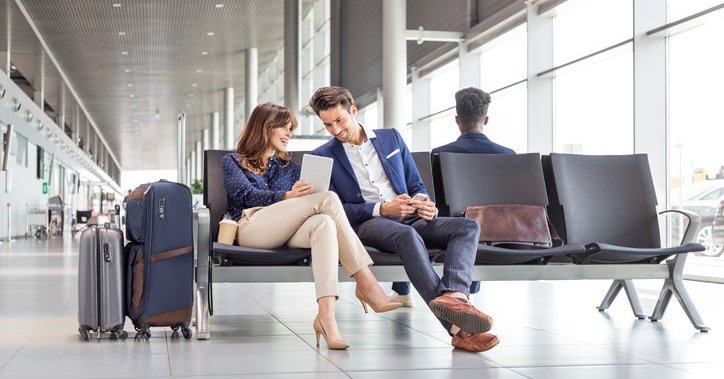 A man and woman sitting at an airport and waiting for their flight while looking at a tablet.