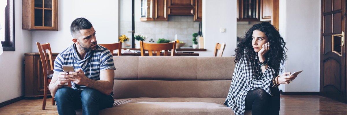 man and woman sitting at opposite ends of a couch and looking upset