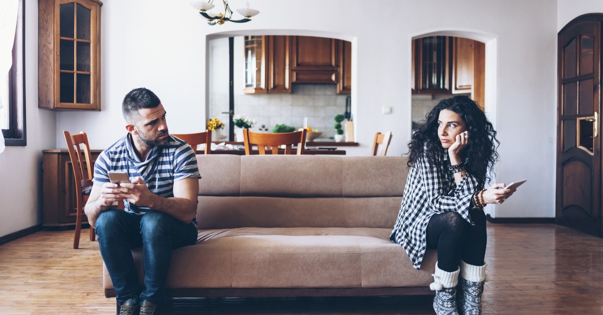 man and woman sitting at opposite ends of a couch and looking upset