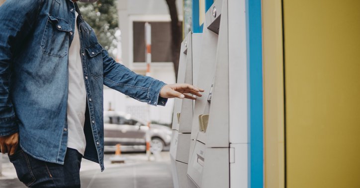 A man wearing a medical mask and taking money out of an ATM on the street.
