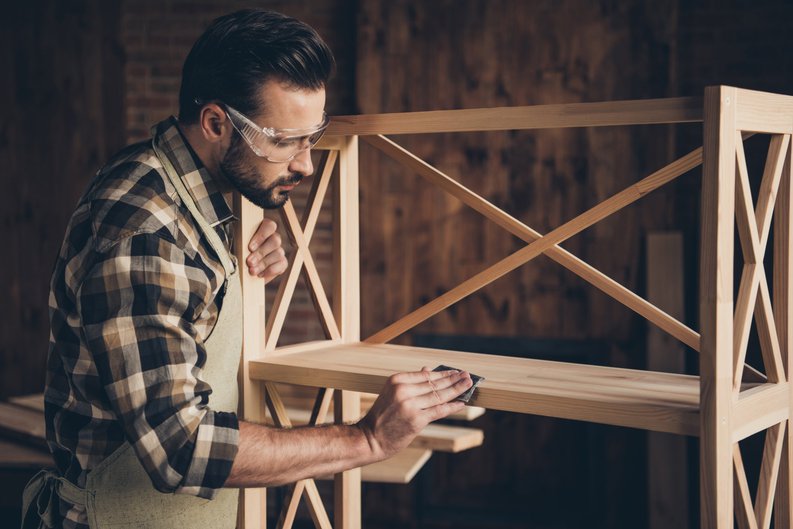 A man building a piece of furniture out of wood in a workshop.