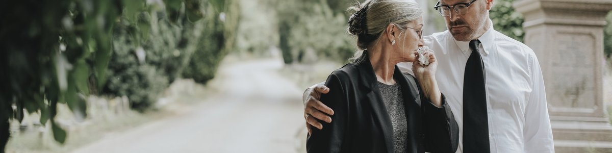A man comforts a tearful woman after a funeral.