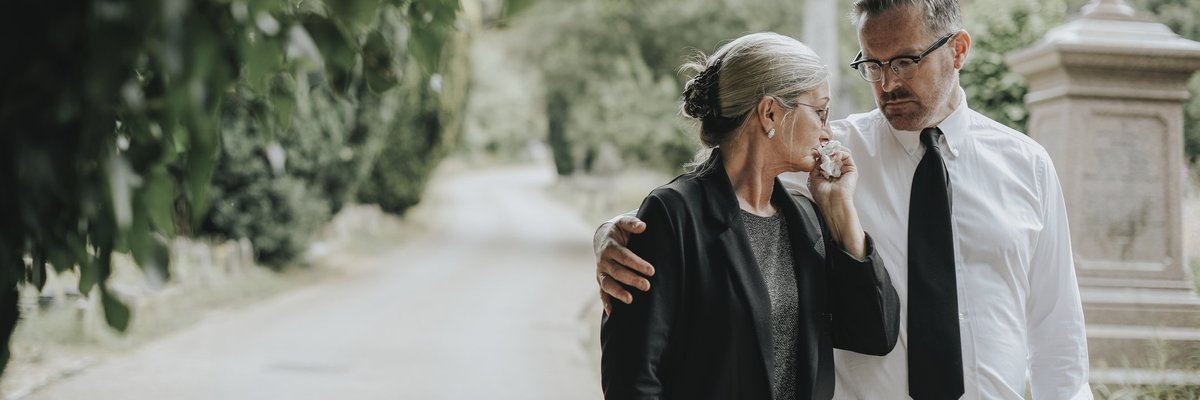A man comforts a tearful woman after a funeral.