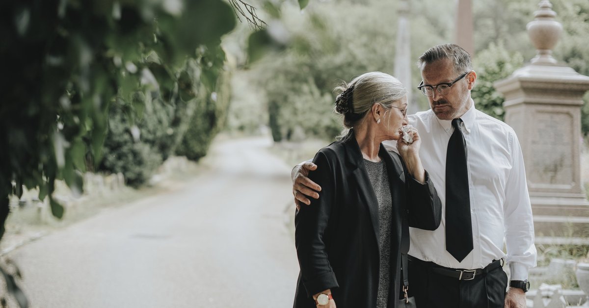 A man comforts a tearful woman after a funeral.