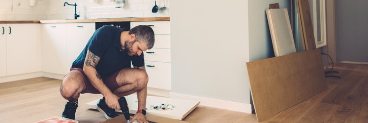 A man drilling cupboard doors while doing renovations in his kitchen.