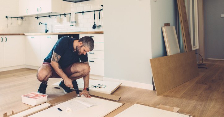 A man drilling cupboard doors while doing renovations in his kitchen.