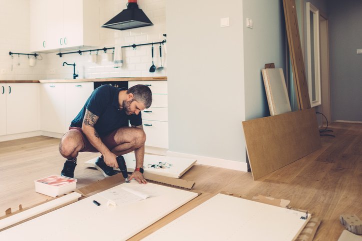 A man drilling cupboard doors while doing renovations in his kitchen.