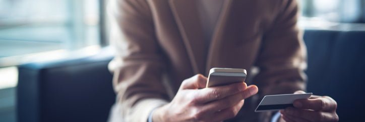 A man sitting on a couch and holding a credit card in one hand and a phone in the other.