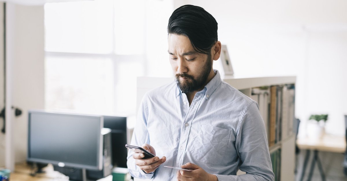 A man standing in an office while holding his phone and a credit card.